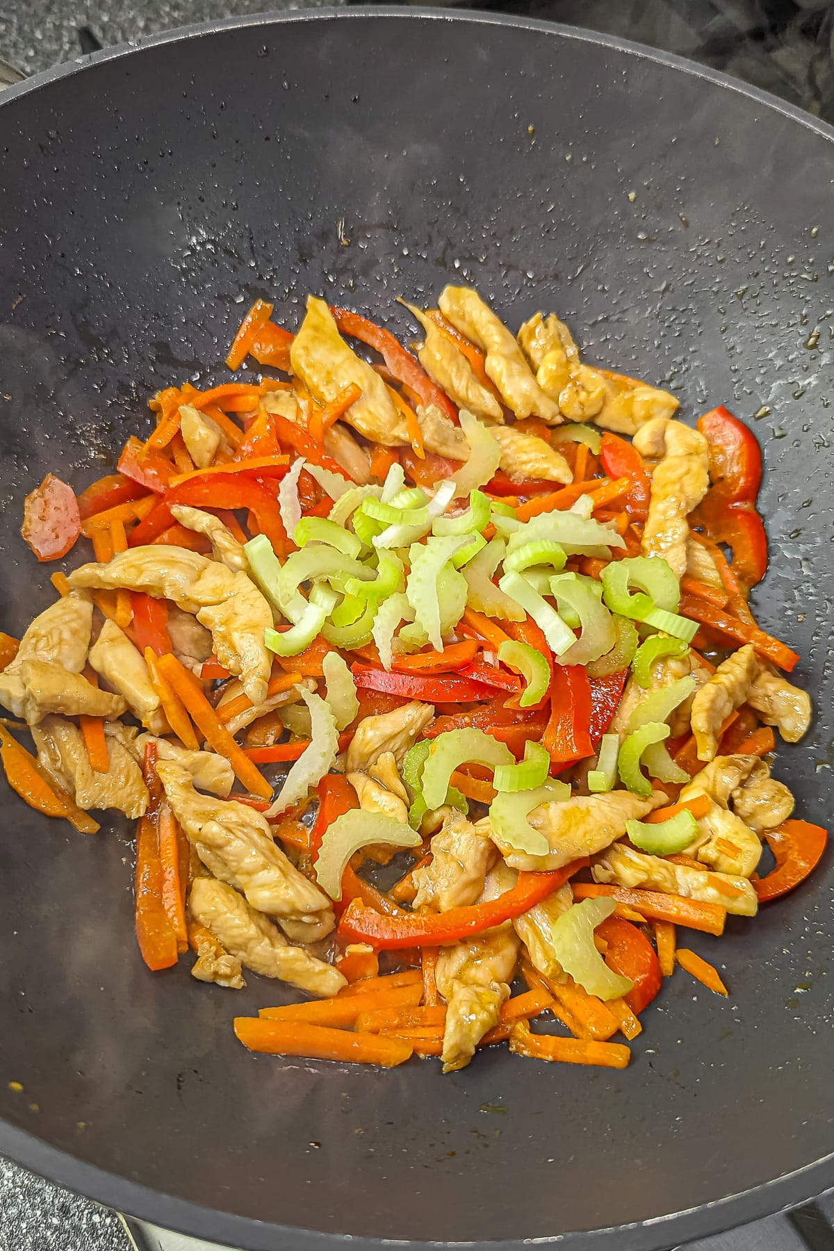 Stir-fry with chicken, red bell pepper, carrots, and celery in a pan.