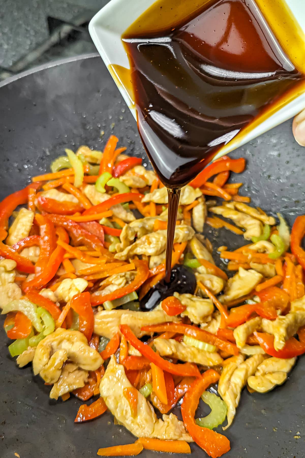Teriyaki sauce being poured over the chicken and vegetable stir-fry in a pan.