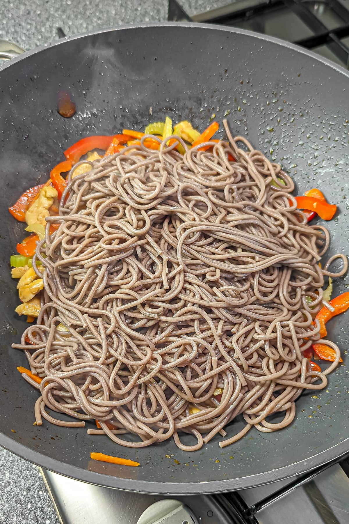 Soba noodles added to the stir-fry in the pan, mixing with the other ingredients.