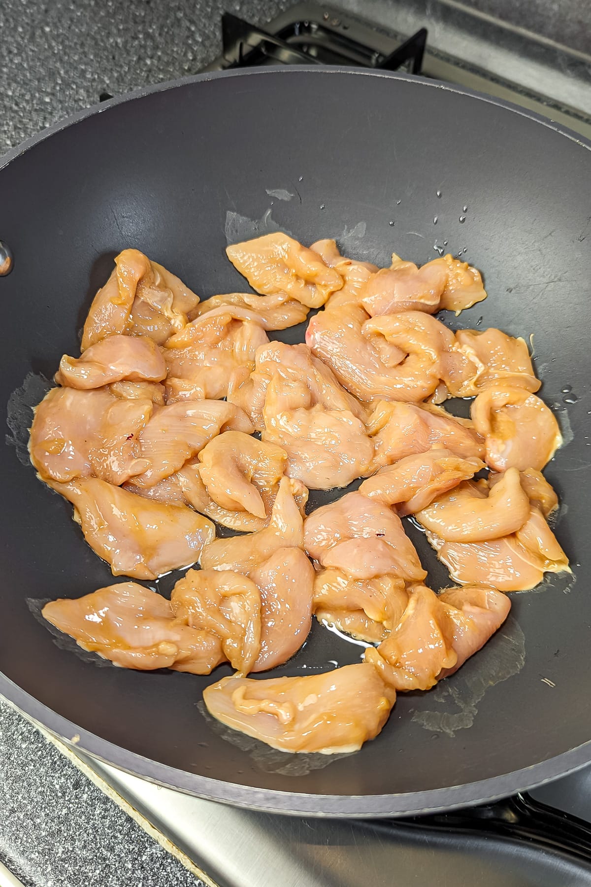 Chicken pieces being cooked in a non-stick pan until golden brown.