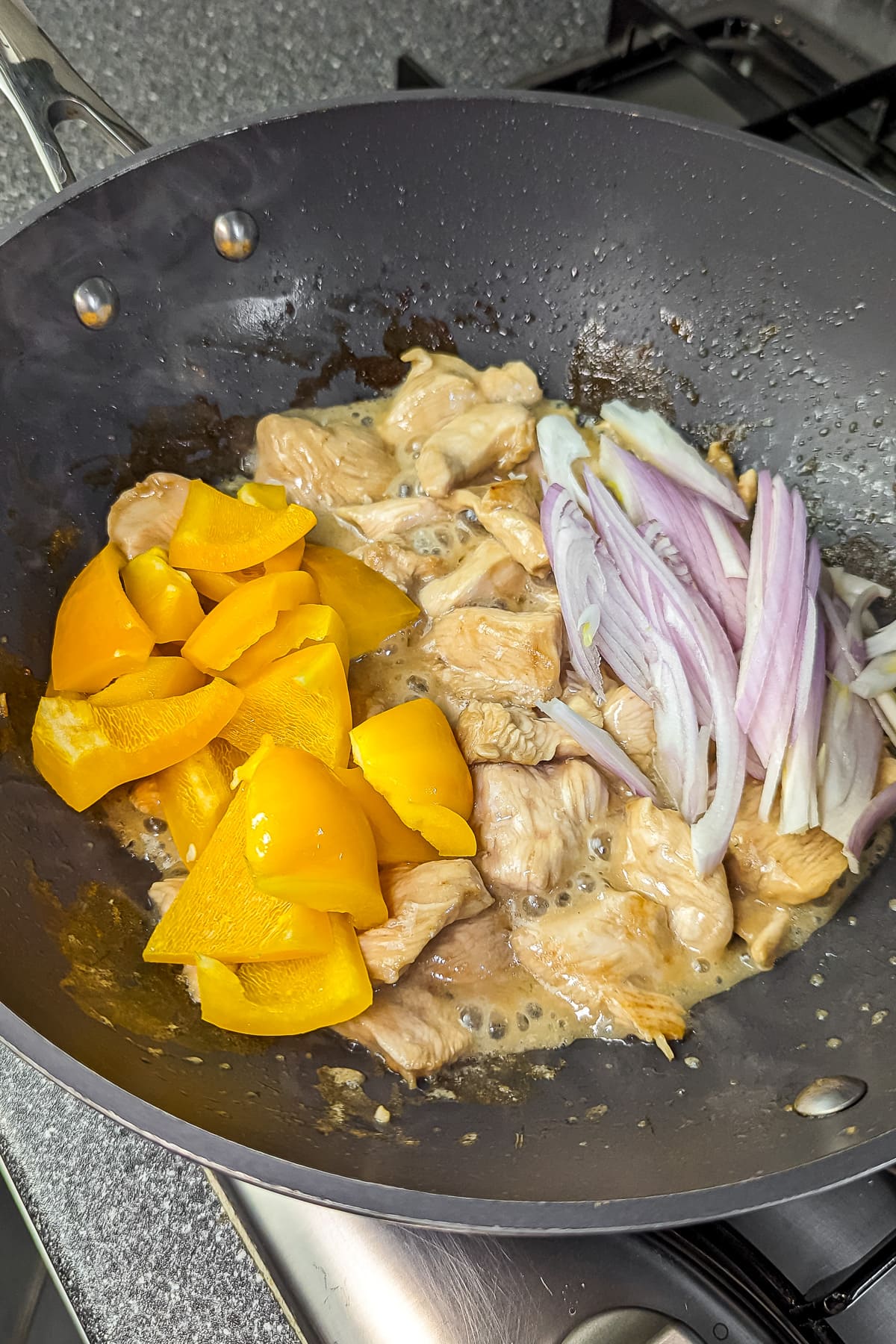 The cooked chicken being tossed with yellow bell pepper strips and red onion in the pan.