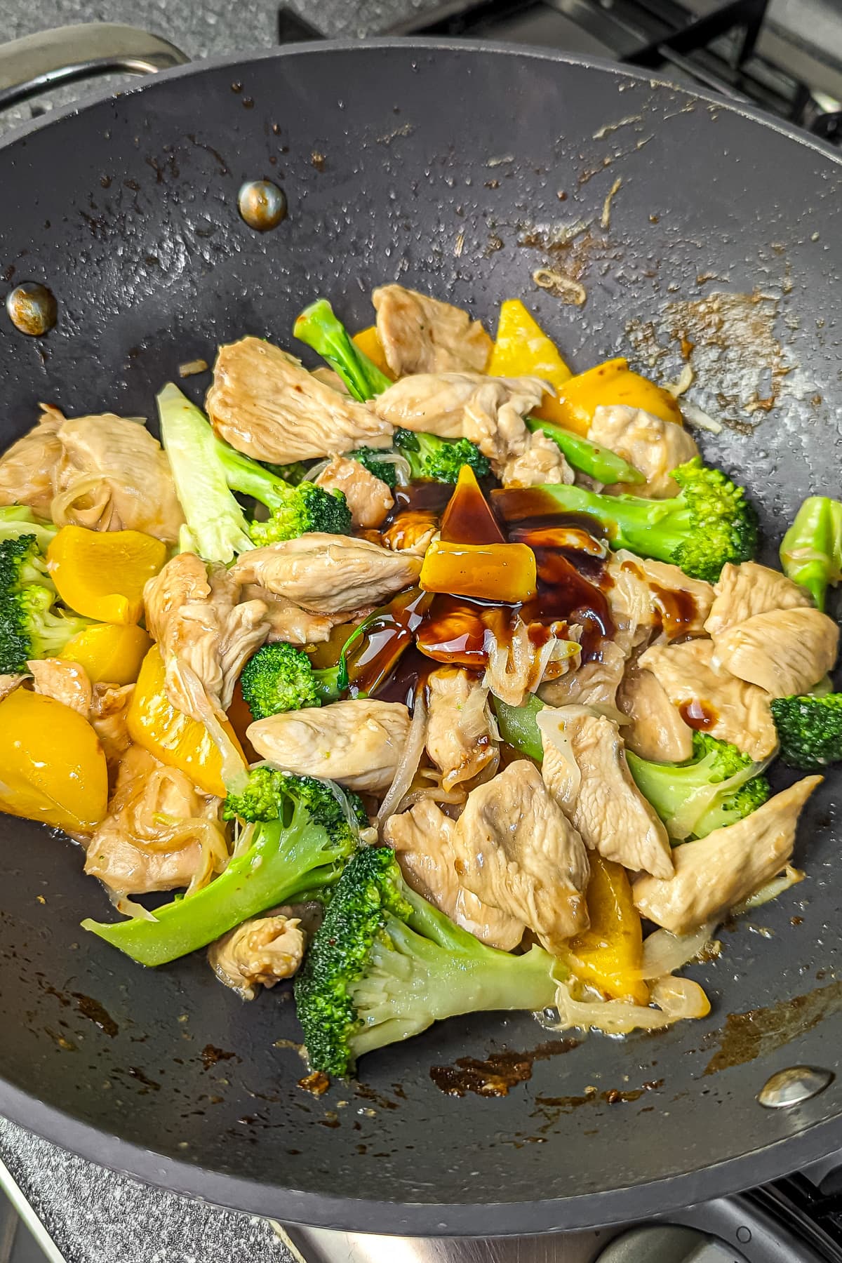 Teriyaki sauce being poured over the chicken and vegetable stir-fry in the pan.