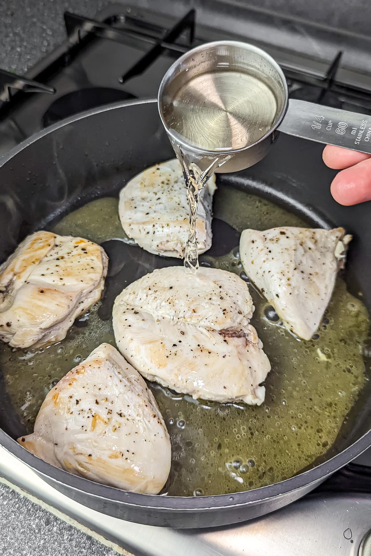 Searing chicken breasts in a skillet with a splash of white wine being added.