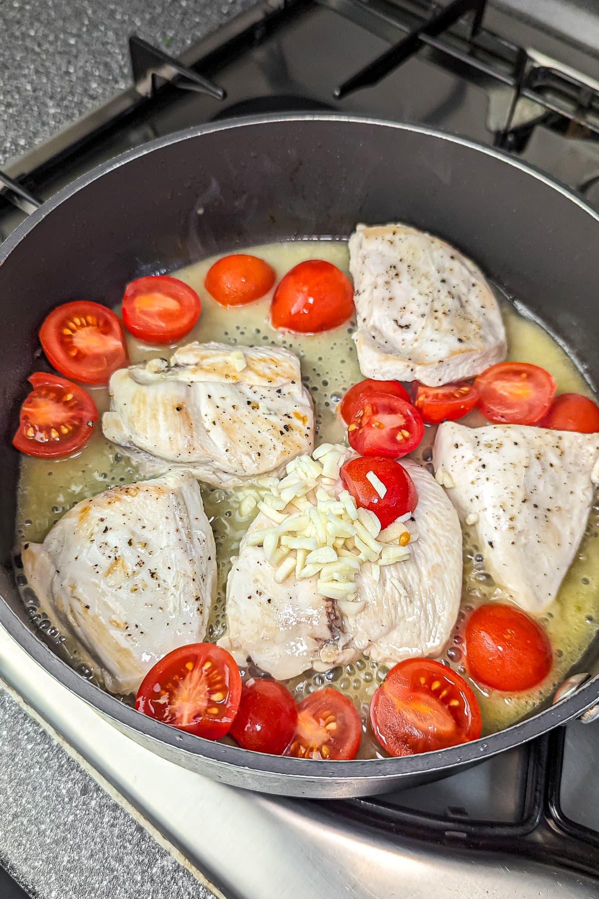 Chicken breasts in a skillet with cherry tomatoes and garlic for a sauce.