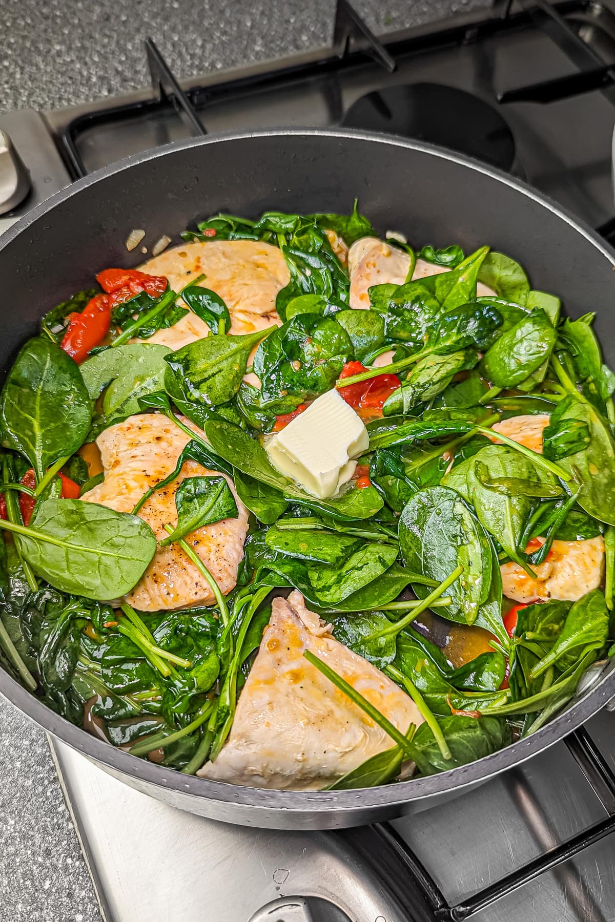 Butter melting into the skillet with chicken, tomatoes, and spinach.