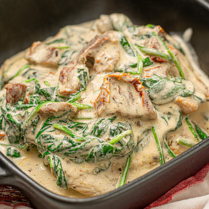 Golden-brown Tuscan chicken in a creamy spinach sauce, served in a skillet on a checkered cloth.