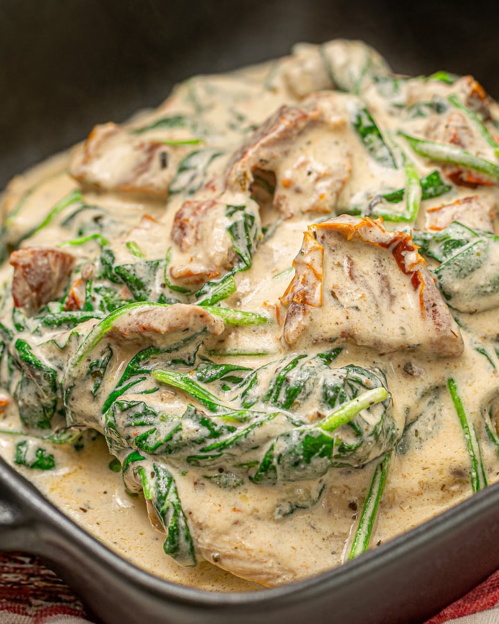 Golden-brown Tuscan chicken in a creamy spinach sauce, served in a skillet on a checkered cloth.