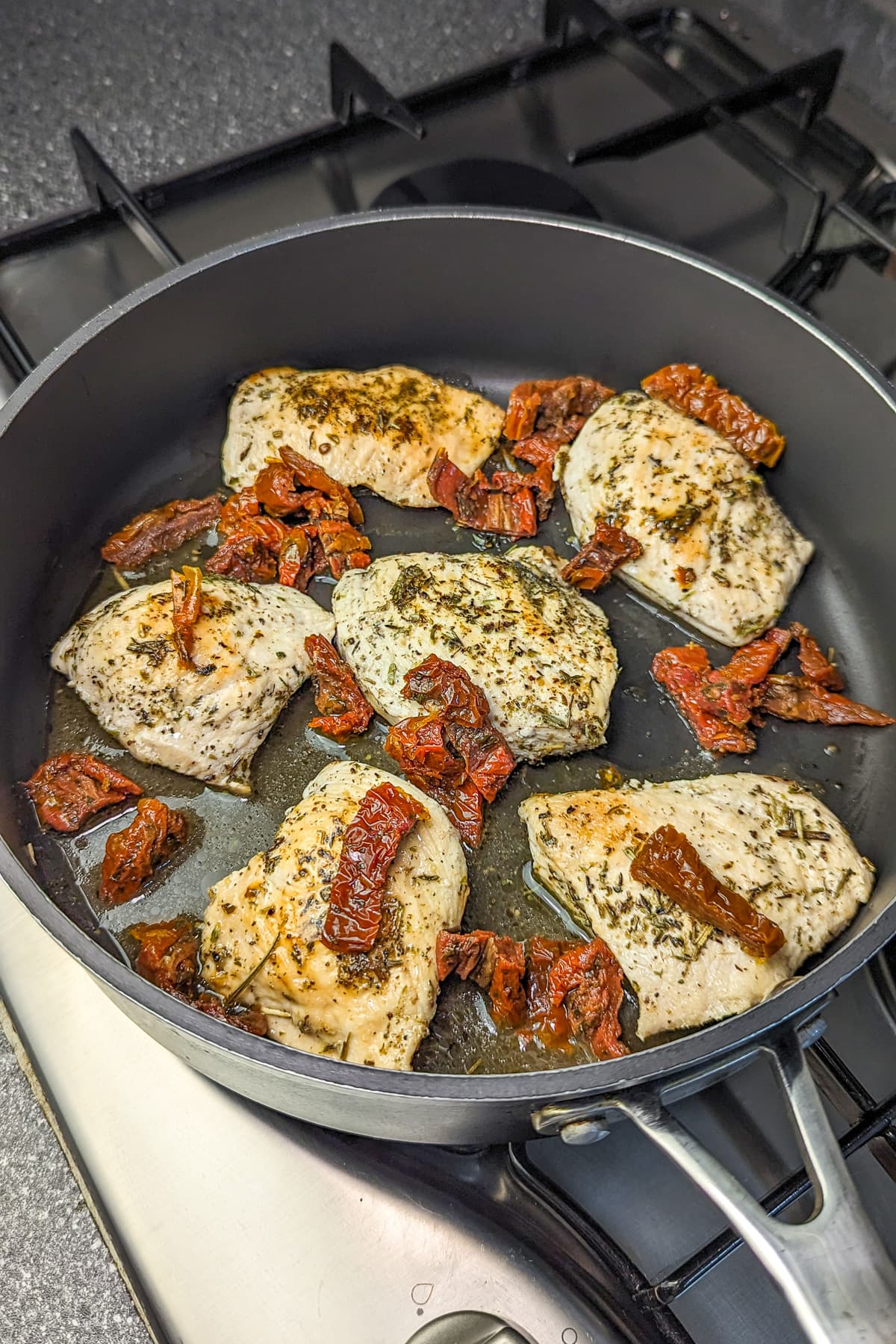 Cooked chicken breasts in a skillet with added sun-dried tomatoes, showing the beginning of a sauce.