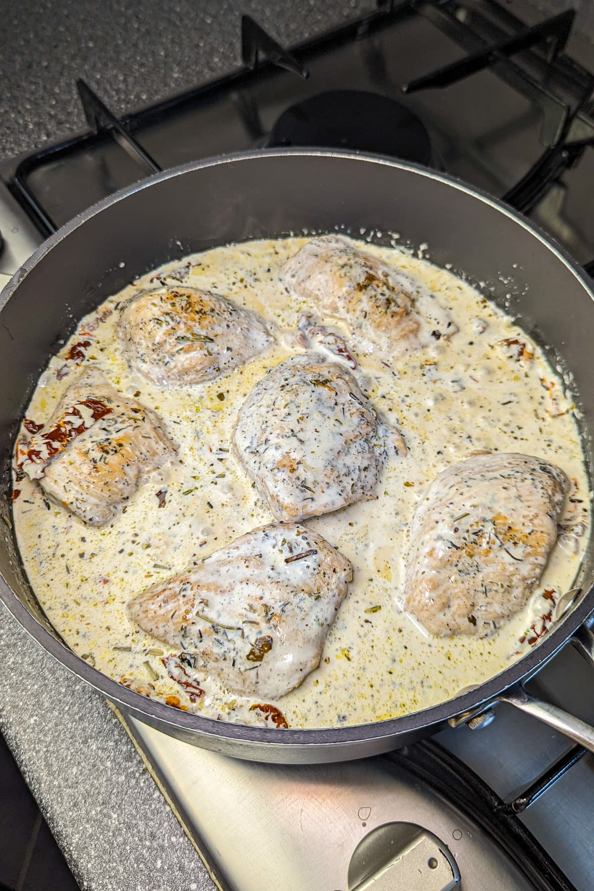 The skillet with chicken and sun-dried tomatoes now also has a creamy sauce added, bubbling around the edges.
