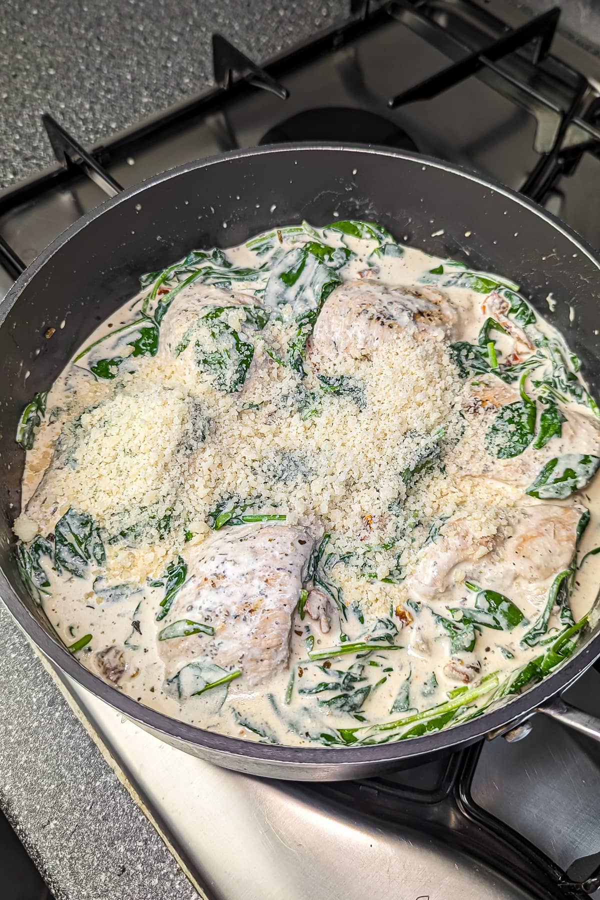 The skillet with Tuscan chicken showing the spinach wilted into the creamy sauce, topped with a sprinkle of Parmesan cheese.